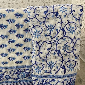 May include: Two white cotton fabric panels with blue floral patterns. The panel on the left has a smaller, repeating pattern of blue leaves and flowers. The panel on the right has a larger, more intricate pattern of blue flowers and vines. Both panels have a blue paisley border.
