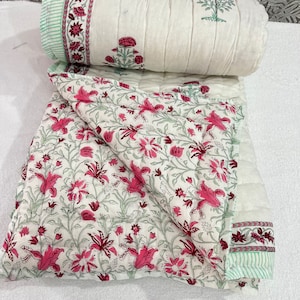 May include: A white cotton quilt with a floral print in shades of pink and green. The quilt is folded in half and has a border with a green and white striped pattern.