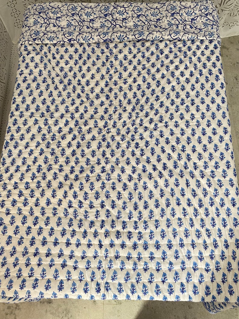 May include: A white cotton quilt with a blue floral pattern. The quilt is quilted in a diamond pattern and has a blue floral border.
