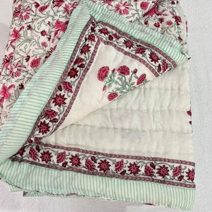 May include: A white cotton quilt with a pink and green floral print. The quilt is folded in half and the floral print is visible on both sides.