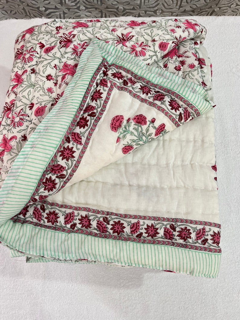 May include: A white cotton quilt with a pink and green floral print. The quilt is folded in half and the floral print is visible on both sides.
