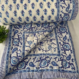 May include: A white and blue cotton quilt with a floral pattern. The quilt is folded in half and has a border of blue stripes.