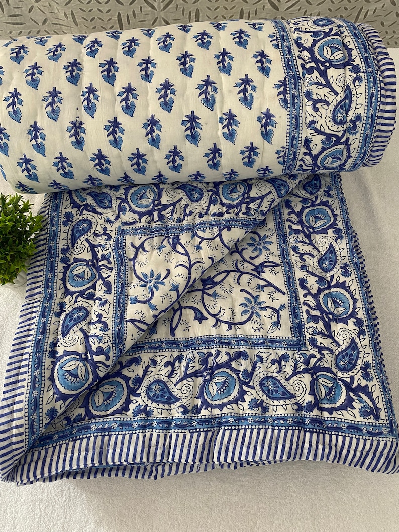May include: A white and blue cotton quilt with a floral pattern. The quilt is folded in half and has a border of blue stripes.