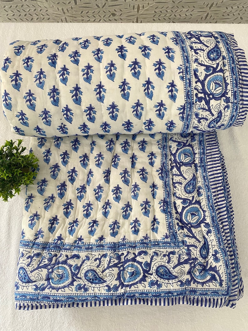 May include: A white cotton quilt with a blue floral pattern. The quilt has a border of paisley designs and a striped border.