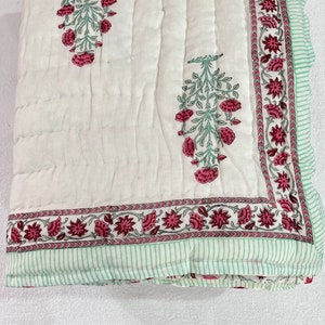 May include: White cotton quilt with a green and pink floral print. The quilt has a border of green and pink flowers and a green and white striped border.