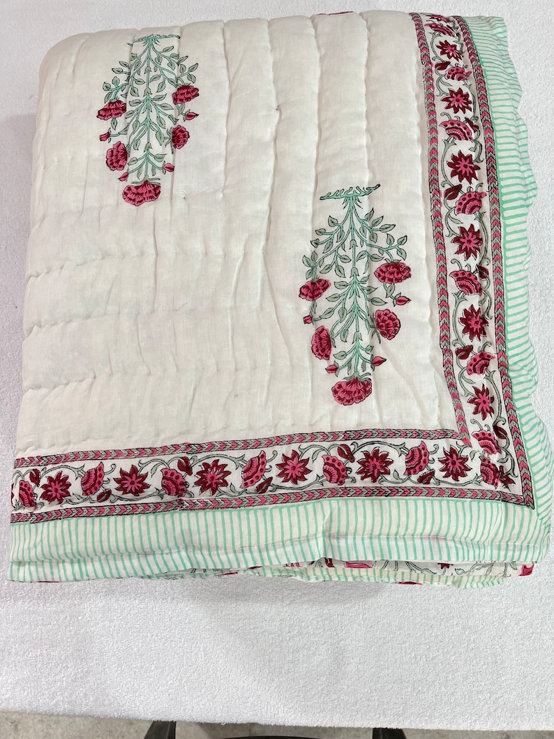 May include: White cotton quilt with a green and pink floral print. The quilt has a border of green and pink flowers and a green and white striped border.