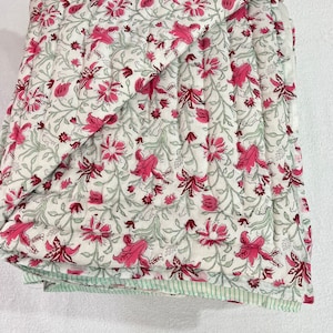 May include: A white cotton quilt with a pink floral pattern. The quilt is folded in half and has a green and white striped border.