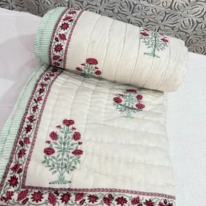 May include: White cotton quilt with a green and pink floral print. The quilt is quilted with a diamond pattern and has a green and white striped border.
