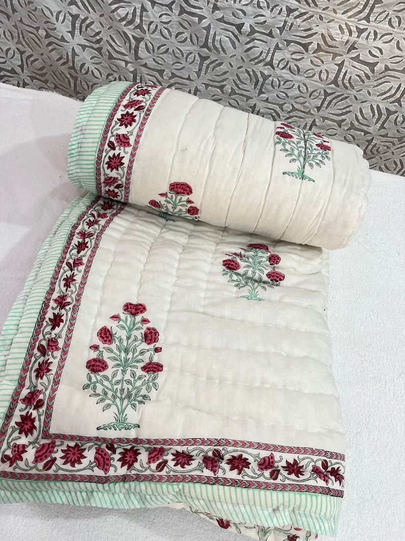 May include: White cotton quilt with a green and pink floral print. The quilt is quilted with a diamond pattern and has a green and white striped border.