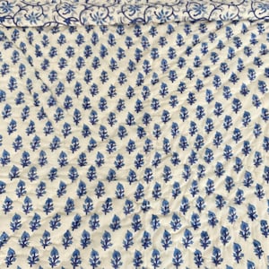 May include: White fabric with a blue floral pattern. The pattern is a repeating design of small blue flowers.