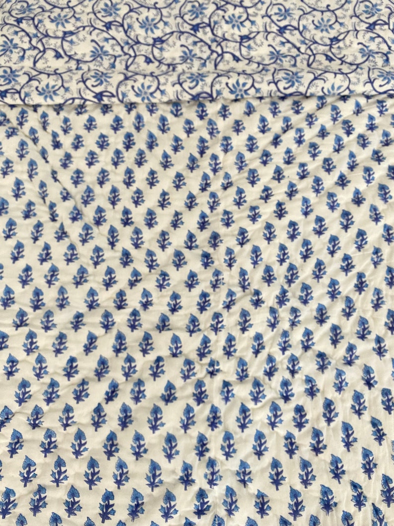 May include: White fabric with a blue floral pattern. The pattern is a repeating design of small blue flowers.