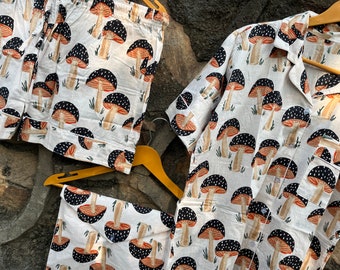 Puede incluir: Un conjunto de pijama blanco con estampado de setas negras y rojas. El conjunto incluye una camisa de manga corta y pantalones cortos.
