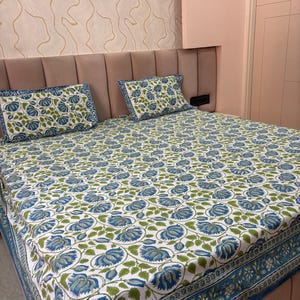 Può includere: Un lenzuolo bianco e due federe con un motivo floreale blu e verde. La biancheria da letto ha un bordo con un motivo floreale ripetuto. Il letto è fatto con le lenzuola e i cuscini.