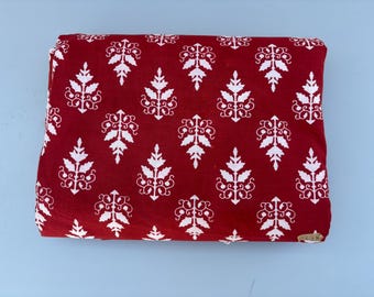 May include: Red fabric with a white floral pattern. The fabric has a repeating pattern of white stylised flowers on a red background.