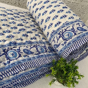 May include: A white and blue cotton quilt with a floral pattern. The quilt is folded in half and has a border of blue and white stripes.