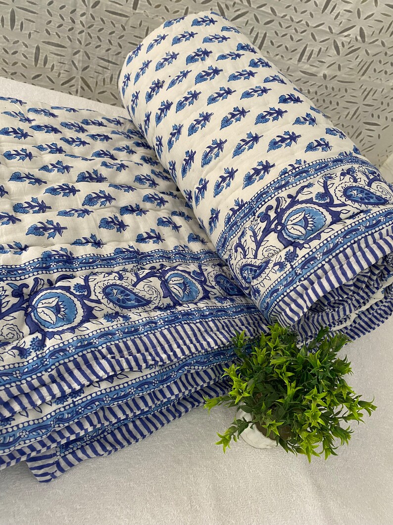 May include: A white and blue cotton quilt with a floral pattern. The quilt is folded in half and has a border of blue and white stripes.