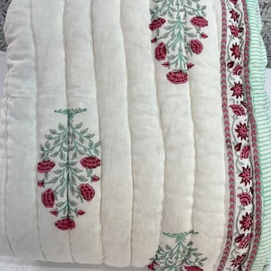 May include: White cotton quilt with a green and pink floral print. The quilt has a quilted design and a border with a repeating floral pattern.