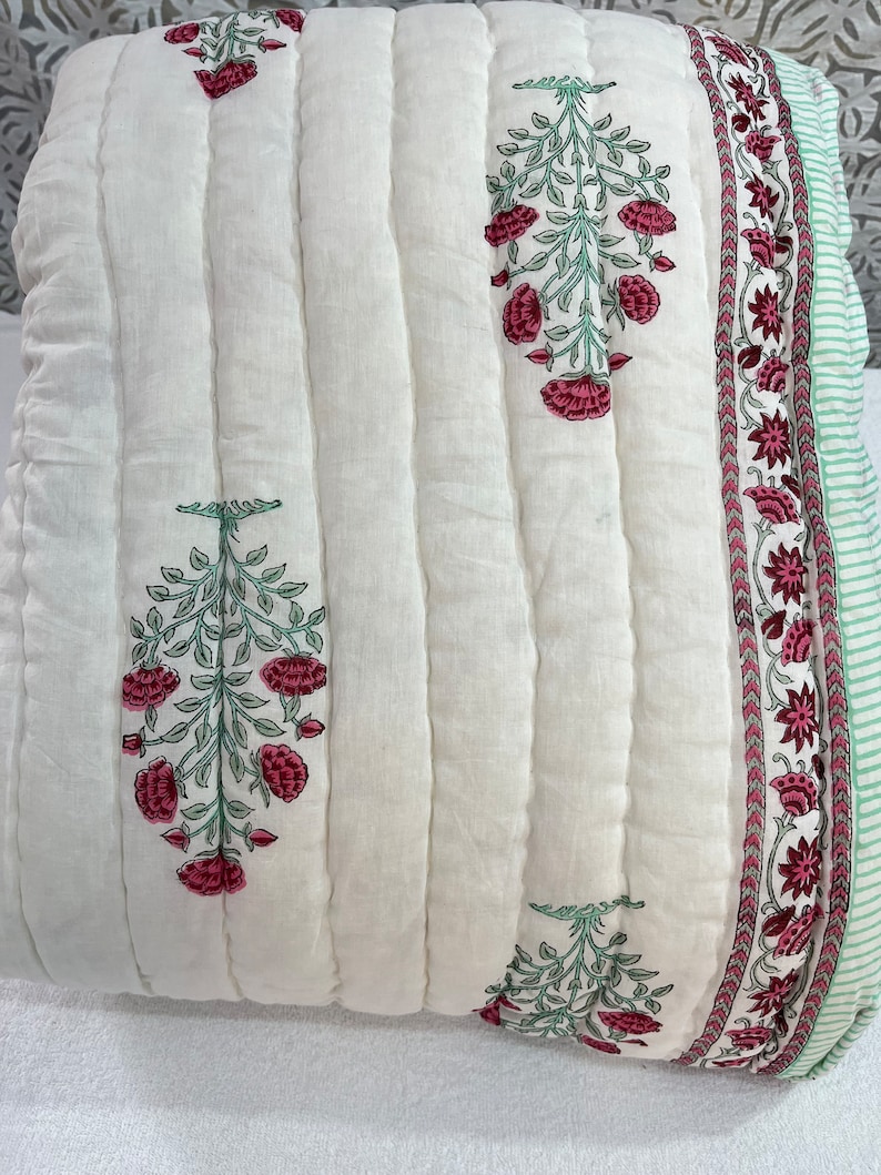 May include: White cotton quilt with a green and pink floral print. The quilt has a quilted design and a border with a repeating floral pattern.