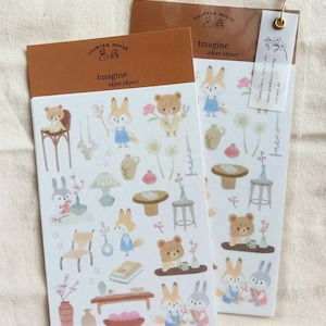 May include: Two sticker sheets with a brown header that reads "SOURTEA HOUSE" and "Imagine objet object." The stickers feature illustrations of animals, furniture, and plants in soft colors. One sheet has a tag with text.