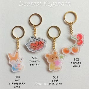 May include: A collection of acrylic keychains with gold-colored hardware. The keychains feature various designs, including a fox with a strawberry cake, a tomato basket, a bear with a pink star, and tomato veins. The text "Dearest Keychain" is at the top.