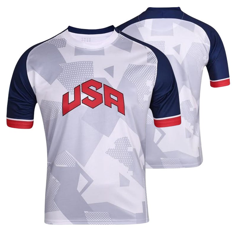 K&ouml;nnte beinhalten: Wei&szlig;es Sport-T-Shirt mit geometrischem Muster und dem Wort "USA" in roten Blockbuchstaben. Das Shirt hat marineblaue &Auml;rmel mit roten Abschl&uuml;ssen. Ein weiteres Shirt ist im Hintergrund zu sehen.