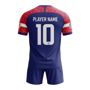 Puede incluir: Un conjunto de camiseta y pantal&oacute;n corto de f&uacute;tbol azul marino. La camiseta muestra el n&uacute;mero 10 en blanco, con el texto "PLAYER NAME" encima. Acentos rojos y blancos adornan los hombros y las mangas. Un peque&ntilde;o gr&aacute;fico de bal&oacute;n de f&uacute;tbol est&aacute; debajo del n&uacute;mero.