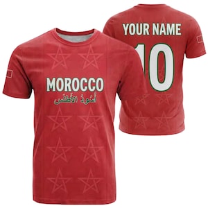 May include: Red soccer jersey with the word "MOROCCO" in white and green, and Arabic text below. The front features star patterns. The back has "YOUR NAME" above the number "10" in white with a green outline. A small flag is on the sleeve.