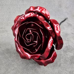 May include: A handcrafted, glossy red rose sculpture with detailed petals and a dark stem. The rose is a vibrant, eye-catching piece, perfect for home decor or as a unique gift. The sculpture is made of metal.