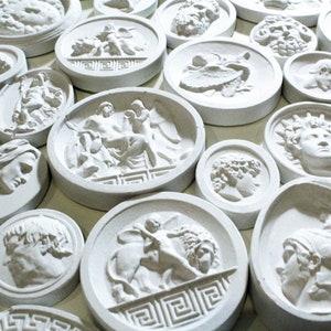 May include: A collection of white plaster round plaques with various raised designs of Greek mythology figures and symbols.