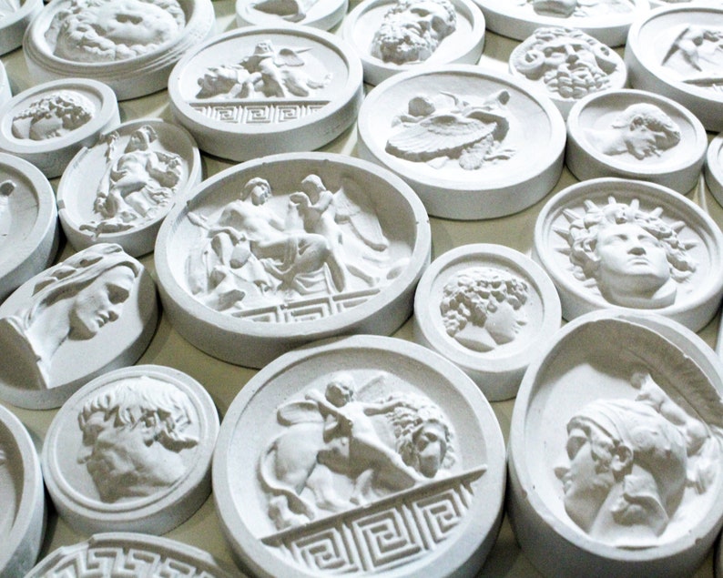 May include: A collection of white plaster round plaques with various raised designs of Greek mythology figures and symbols.