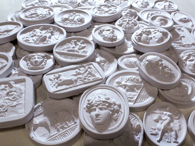 May include: A collection of white plaster relief sculptures featuring various figures and designs. The sculptures are oval and rectangular in shape and have a textured surface.