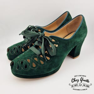 Puede incluir: Un par de zapatos de tacón peep-toe de ante verde oscuro con cierre de cordones. Los zapatos tienen una suela de plataforma y un tacón grueso. El diseño incluye recortes decorativos en la pala. La marca "Chez Yvette" está impresa en el lateral.