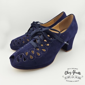 Puede incluir: Un par de zapatos de tacón peep-toe de ante azul marino con cortes decorativos y cordones a juego. Los zapatos tienen un tacón grueso y una suela de plataforma. La marca "Chez Yvette" es visible.