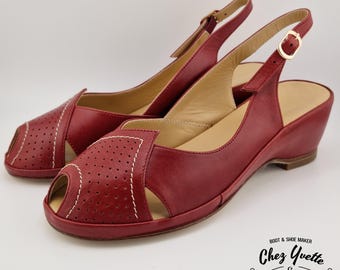 May include: A pair of red leather peep-toe slingback sandals. The sandals feature a perforated design on the vamp, white stitching, and a small wedge heel. The ankle straps have gold-colored buckles. The shoes are displayed on a white background.