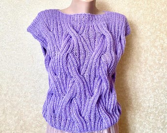 May include: A lilac-coloured, short-sleeved knitted top with a textured cable knit design. The top is displayed on a mannequin and has a round neckline. The bottom of the top is slightly gathered. The top is paired with a light pink skirt.