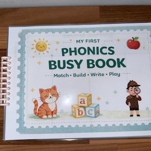 Puede incluir: Un libro de actividades educativo con encuadernación en espiral titulado My First Phonics Busy Book: Match, Build, Write, Play. La portada muestra un sol sonriente, una manzana roja, un gato atigrado naranja, bloques de letras y un detective con lupa.