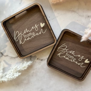 May include: Two square wooden boxes with a clear glass top. The boxes are engraved with the words "Dimes from Heaven" and a small heart.