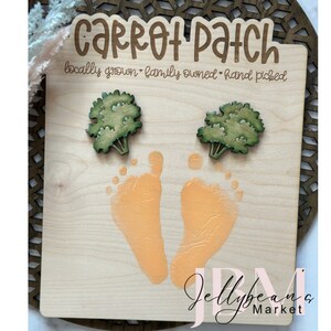 Peut inclure: Panneau en bois avec le texte "Carrot Patch" et les mots "locally grown - family owned - hand picked". Le panneau comporte également deux empreintes de mains orange et deux fanes de carottes vertes.