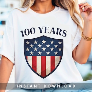 Op de afbeelding: Wit T-shirt met een schildontwerp. Het schild heeft een blauwe achtergrond met witte sterren en rood-witte strepen. De tekst "100 YEARS" staat boven het schild en "INSTANT DOWNLOAD" staat eronder.
