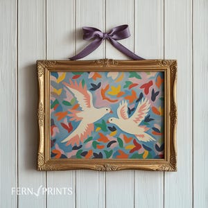 May include: A gold framed print of two white doves flying against a blue background with colorful abstract shapes. The doves are facing each other and have pink accents on their wings.