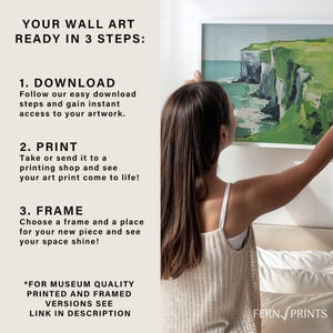 May include: A woman is hanging a framed print of a landscape painting on a wall. The print features a green cliff with a blue ocean in the background. The text on the wall reads "Your Wall Art Ready in 3 Steps: 1. Download 2. Print 3. Frame *For Museum Quality Printed and Framed Versions See Link in Description FERN PRINTS".