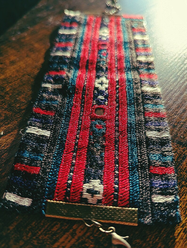 May include: A close-up of a colorful woven bracelet with red, blue, and white stripes. The bracelet has a metal clasp and a brown leather strap.