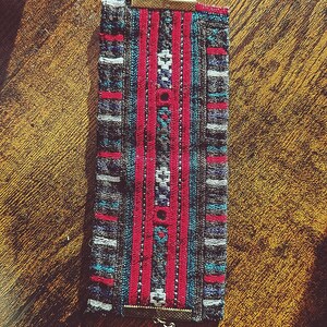 May include: A woven fabric bracelet with a chain and clasp closure. The bracelet features a colorful geometric pattern in shades of red, blue, and gray.