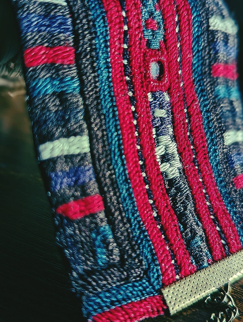 May include: Close-up of a woven fabric with a blue, red, and white geometric pattern. The fabric has a textured surface and is made of tightly woven threads.