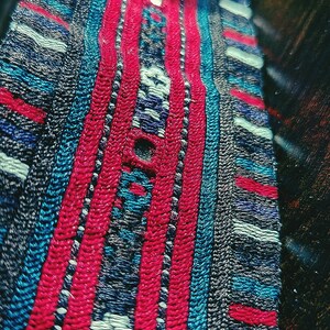 May include: Close-up of a woven fabric with a repeating pattern of red, blue, and white stripes. The fabric has a textured surface and a slightly blurred background.