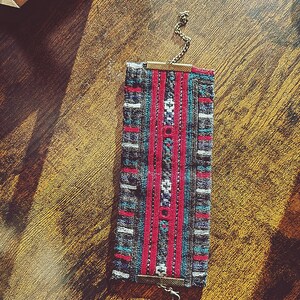 May include: A woven fabric bracelet with a geometric pattern in shades of gray, blue, red, and white. The bracelet has a metal clasp and chain.