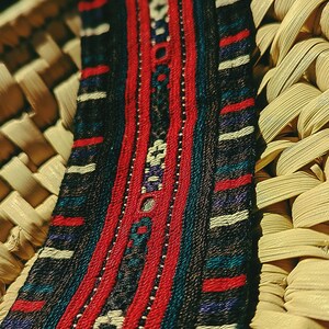 May include: A woven bracelet with a red, blue, and white geometric pattern. The bracelet has a gold metal clasp.