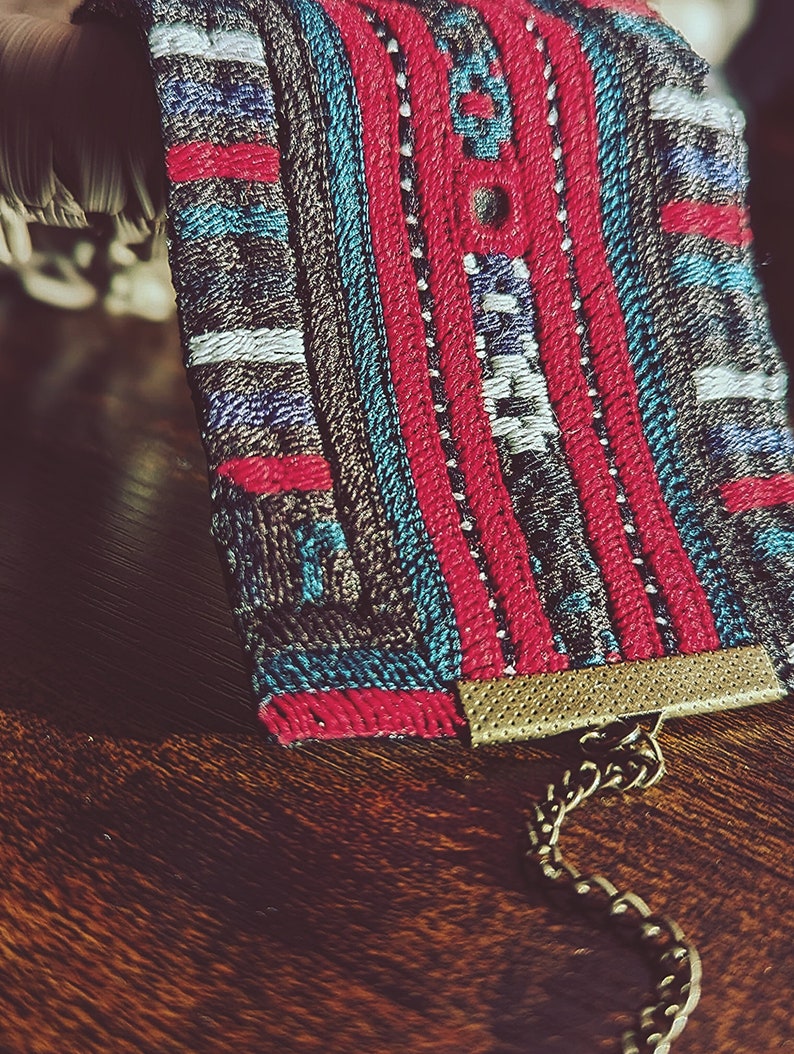 May include: A colorful woven fabric bracelet with a gold chain and clasp. The bracelet features a geometric pattern in shades of red, blue, and white.