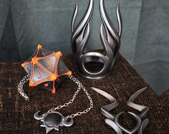 May include: A set of accessories including a black and orange geometric polyhedral object, a silver-toned metallic crown-like headpiece with curved spikes, a silver chain necklace with a black circular pendant, and a silver-toned metallic emblem.