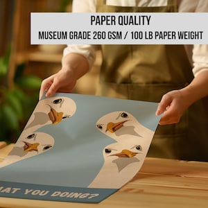 May include: A poster featuring a cartoon design of four white seagulls with orange beaks and black eyes on a light blue background. The text "WHAT YOU DOING?" is at the bottom. The poster is held by a person. The text "PAPER QUALITY MUSEUM GRADE 260 GSM / 100 LB PAPER WEIGHT" is at the top.